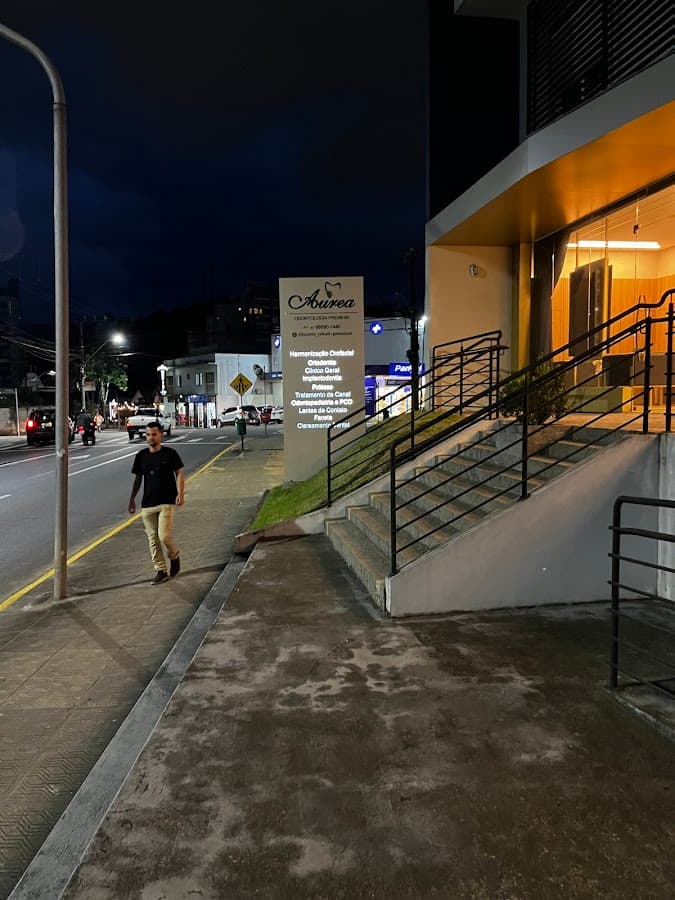 Vista externa da clínica odontológica com iluminação noturna e sinalização visível.